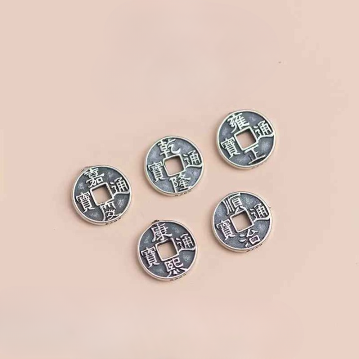 Les cinq sapèques Feng Shui en argent disposées côte à côte, montrant les détails des caractères gravés.