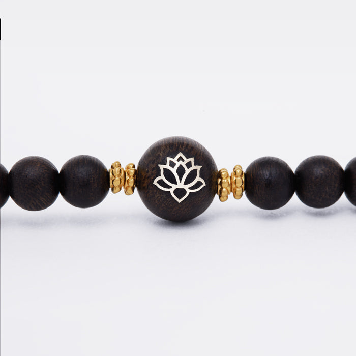 Élément central en bois d’agar incrusté d’or avec motif de fleur stylisée.