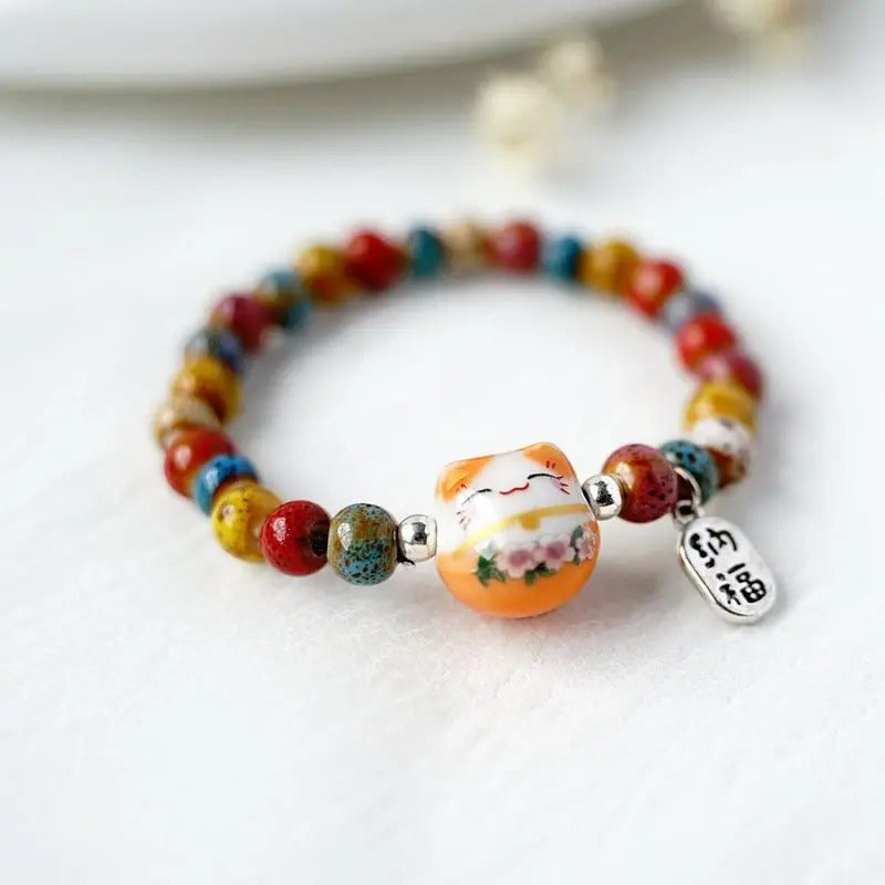 La breloque ovale argentée accompagne le chat porte-bonheur japonais dans un bijou symbolique au style doux et coloré.