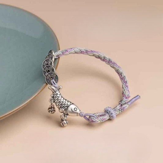 Bracelet carpe Koi et sapèques Feng Shui posé à plat sur fond beige, cordon tressé lilas et crème bien visible.