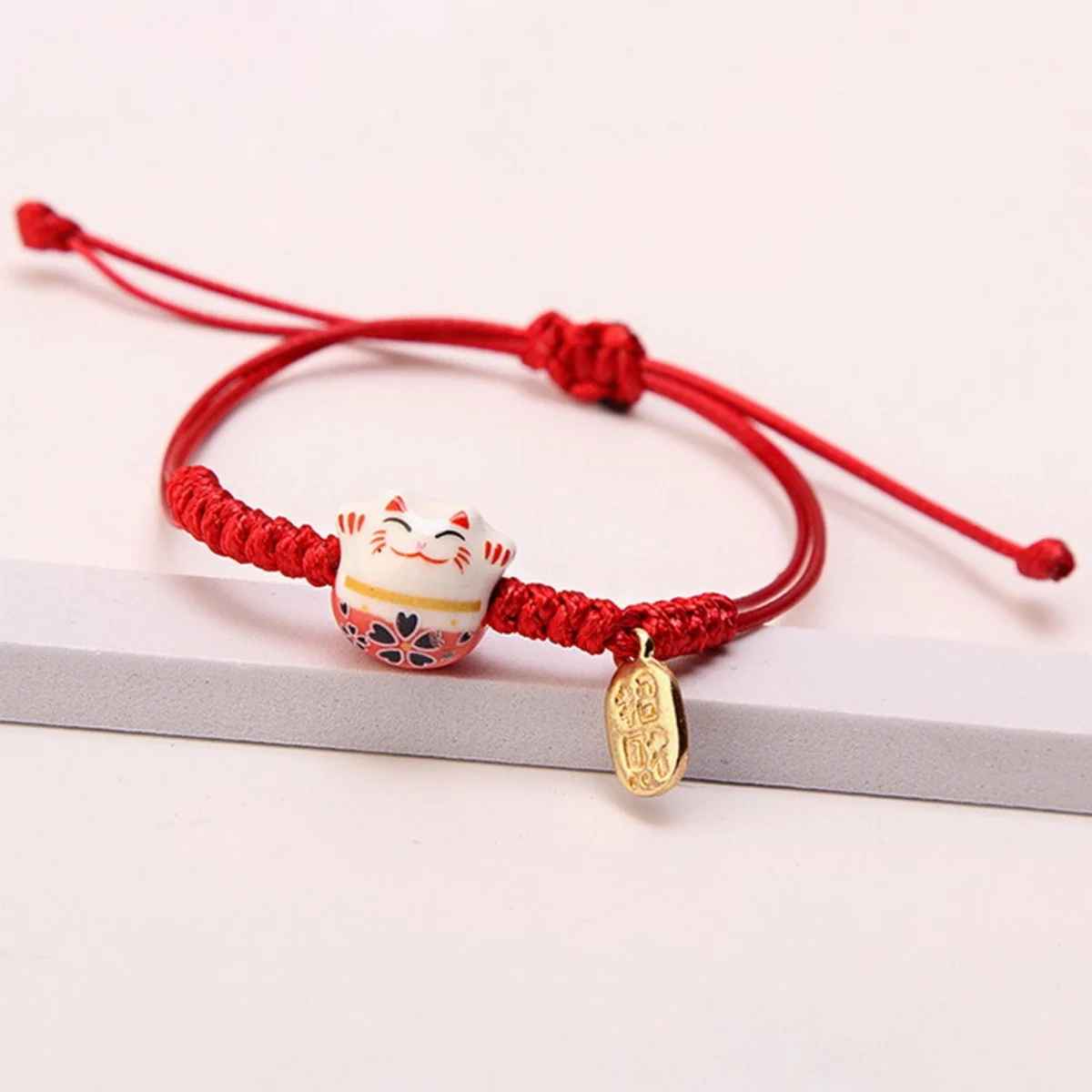Bracelet rouge en macramé avec pendentif Maneki Neko en céramique et grelot doré.