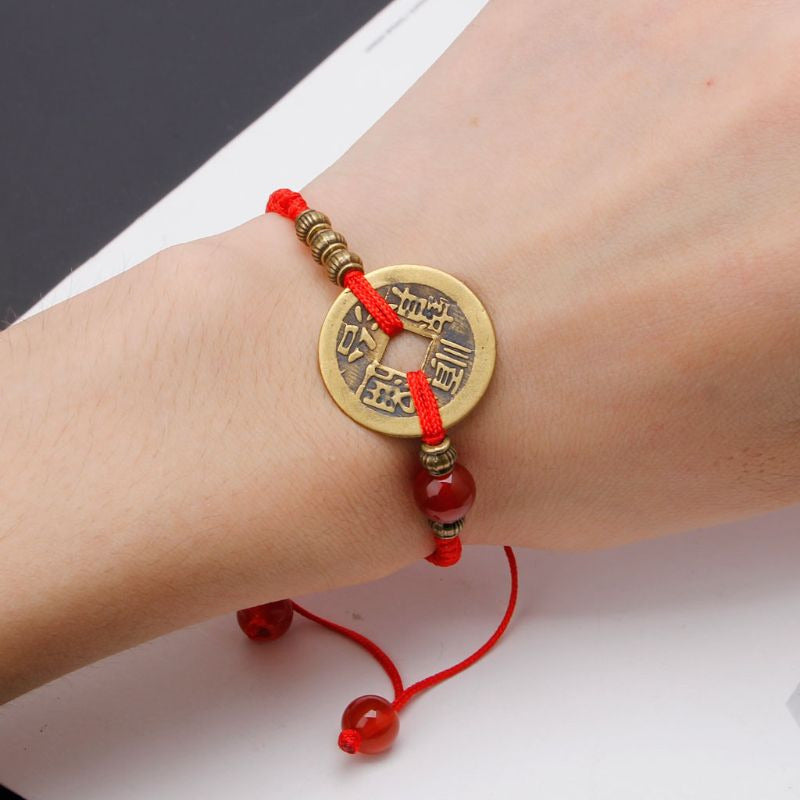 Bracelet Feng Shui rouge porté au poignet avec sapèque dorée centrale.