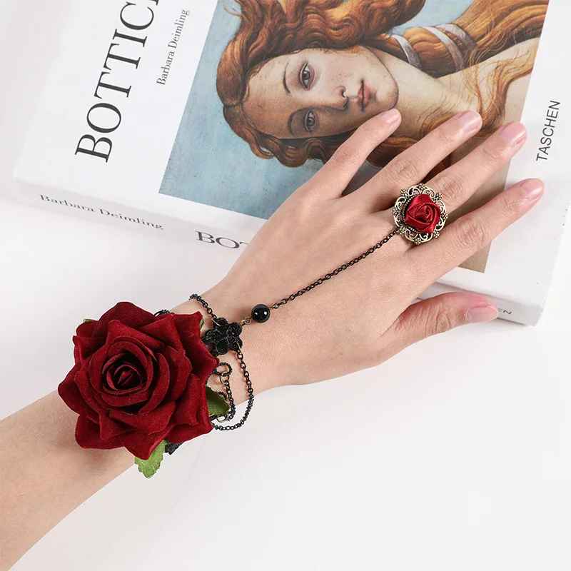 Bracelet en dentelle noire posé sur la main, orné d’une rose rouge et de chaînes fines.