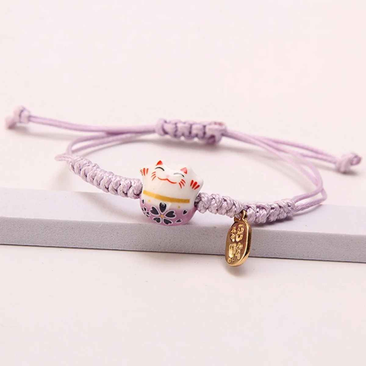 Bracelet tressé rouge avec petit chat japonais souriant et grelot doré.