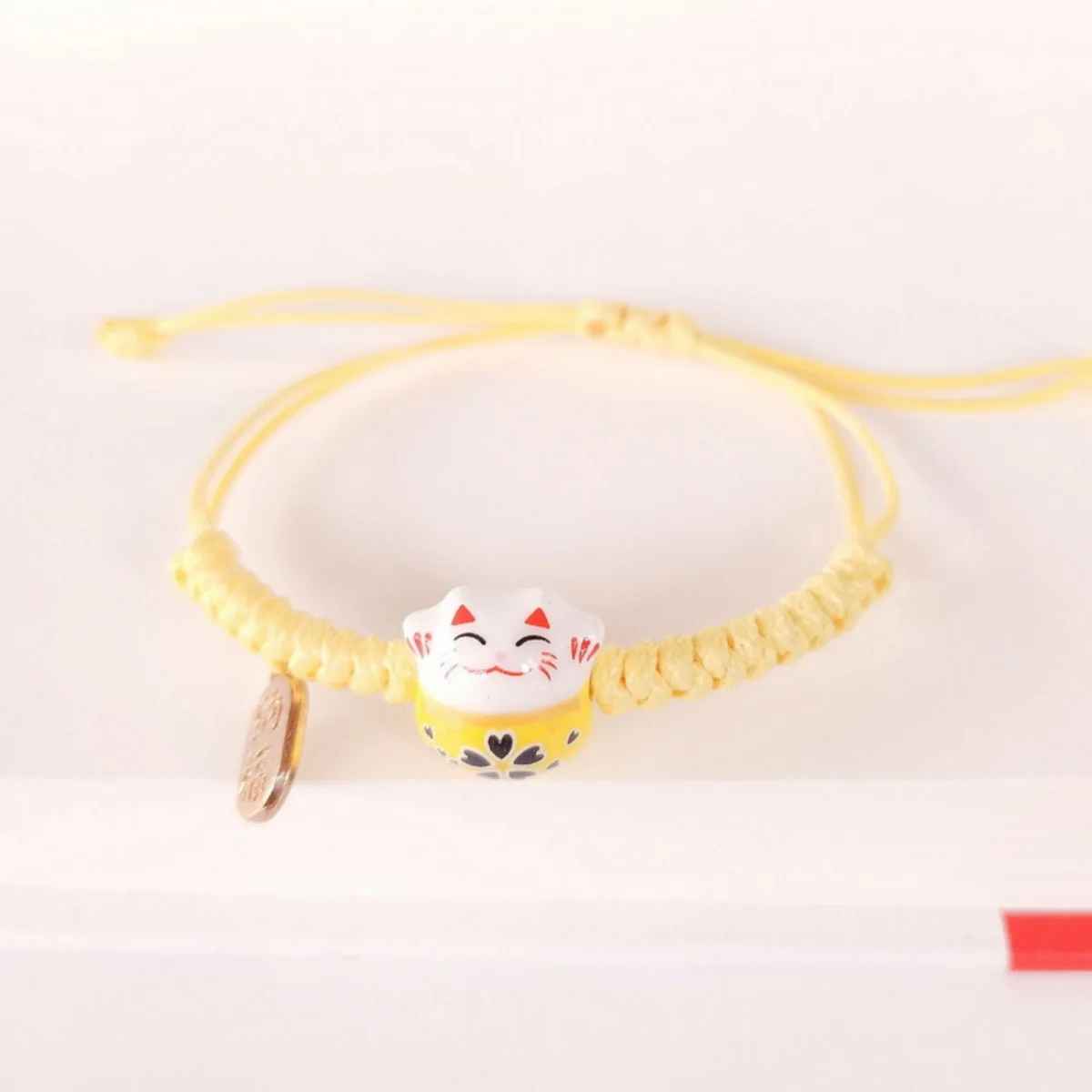 Bracelet artisanal en macramé rouge avec figurine de chat japonais en céramique.