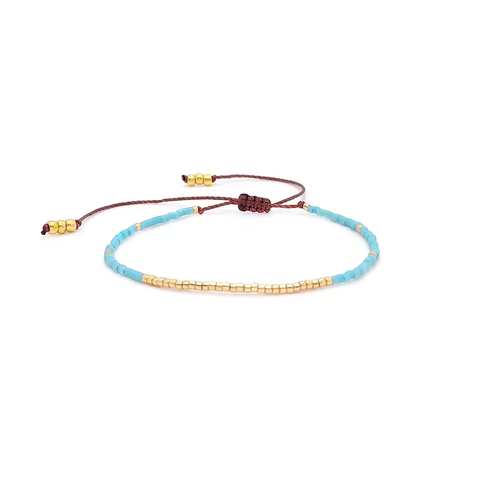 Bracelet minimaliste en perles Miyuki beige posé sur un tissu neutre.