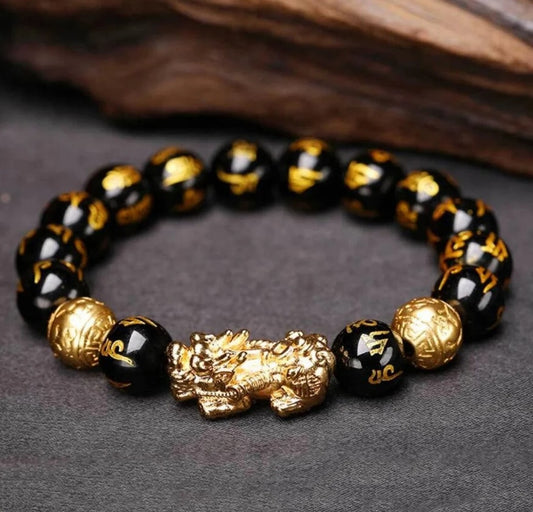 Bracelet feng shui en perles noires avec Pixiu doré posé sur surface sombre.