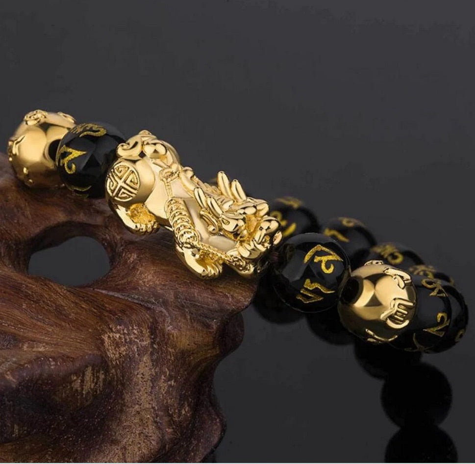 Bracelet Pixiu doré et perles noires présenté en cercle sur fond gris texturé.