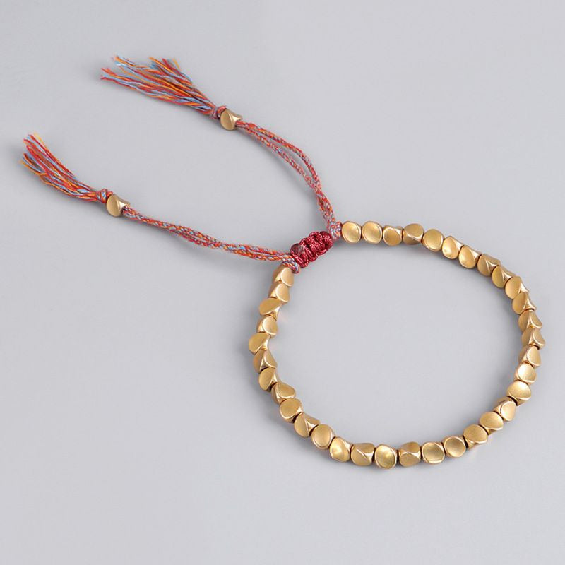 Bracelet porte-bonheur en perles dorées avec cordon macramé multicolore traditionnel.