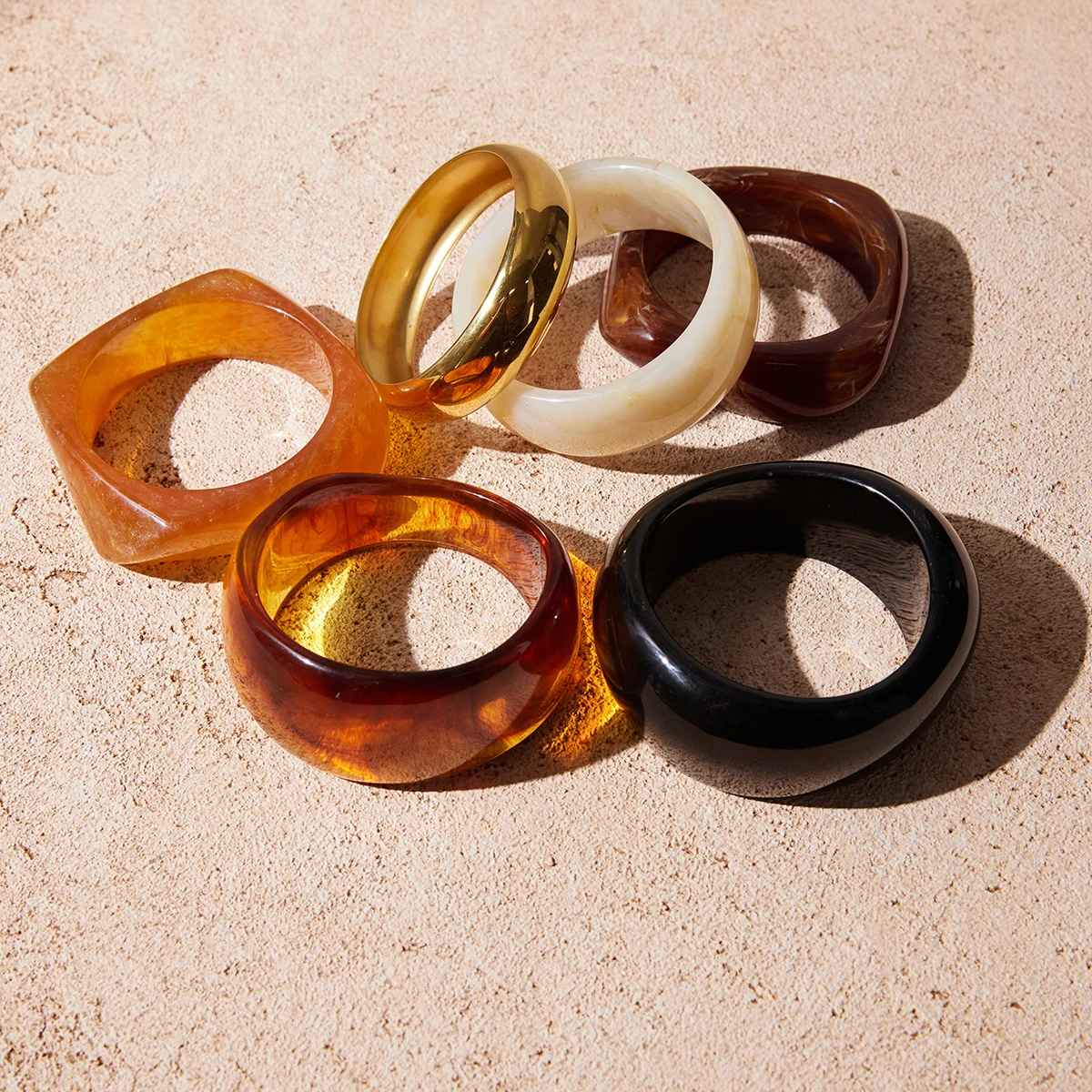 Plusieurs bracelets en résine empilés, aux teintes ambre, ivoire, noir et gold, montrant les variations de formes.