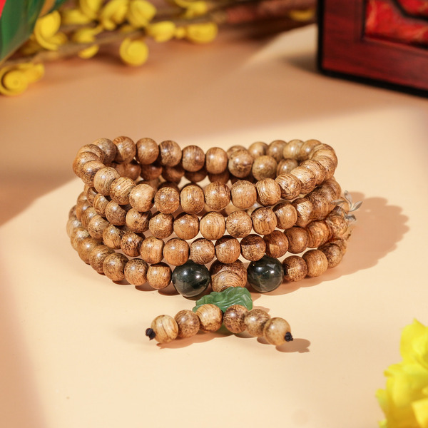 Charm lotus sculpté en pierre naturelle associé à un mala en bois d’agar. Le détail central structure la composition.