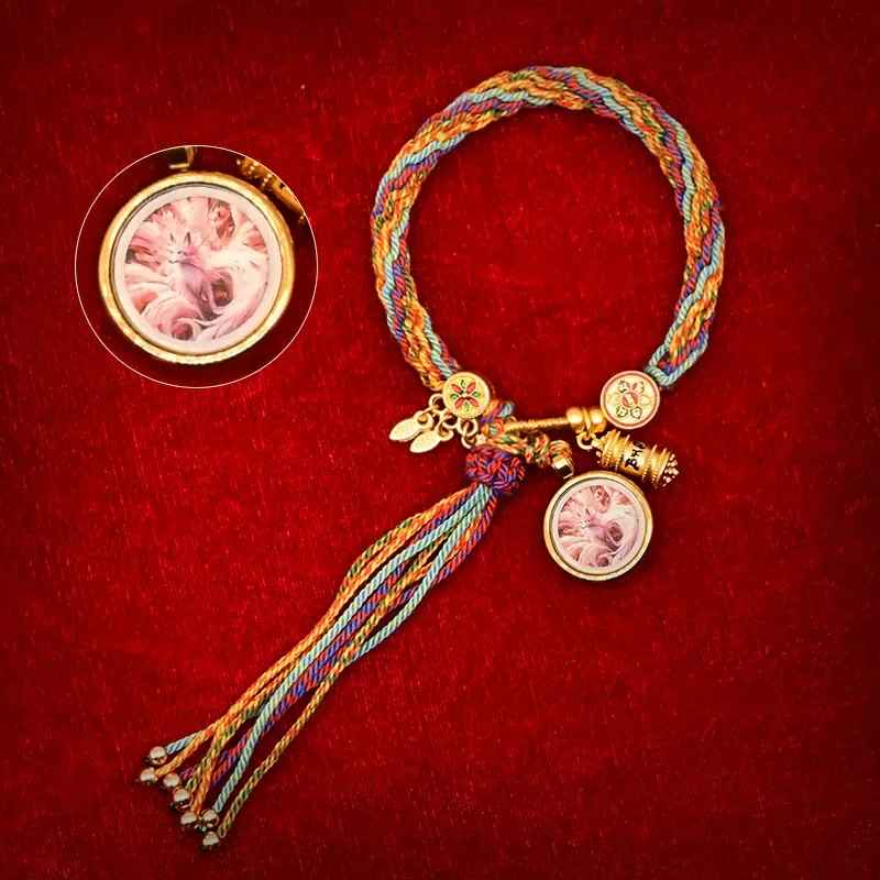 Petite roue de prière dorée attachée au cordon multicolore.